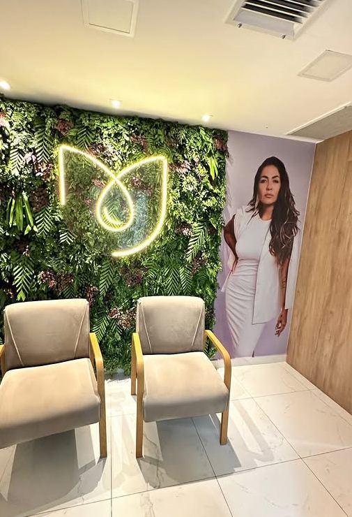 Recepção com parede de plantas, logo em neon e duas poltronas