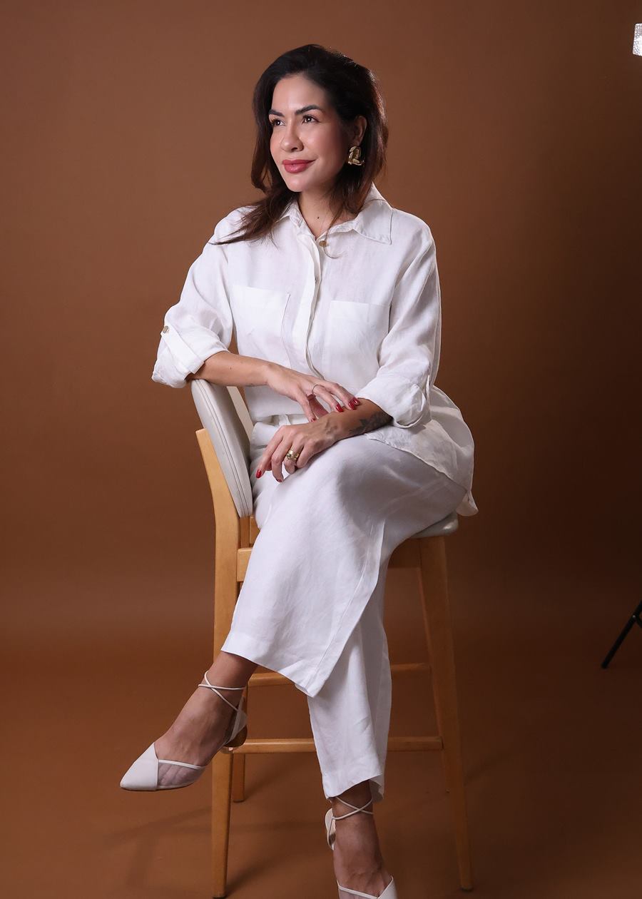 Dra. Mayara Justo sentada em banqueta de madeira, vestindo branco