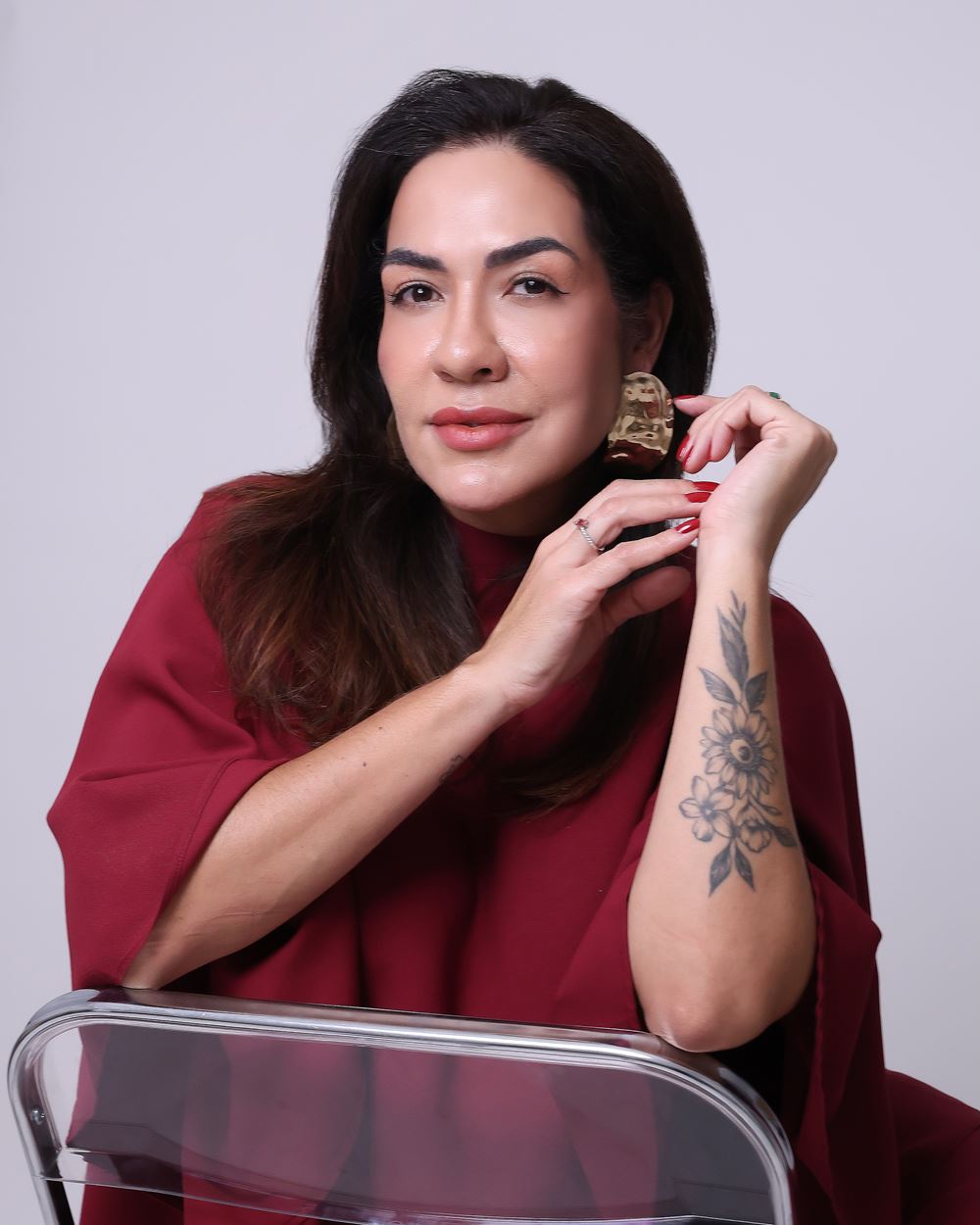 Retrato da Dra. Mayara Justo vestindo vinho, com as mãos próximas ao rosto